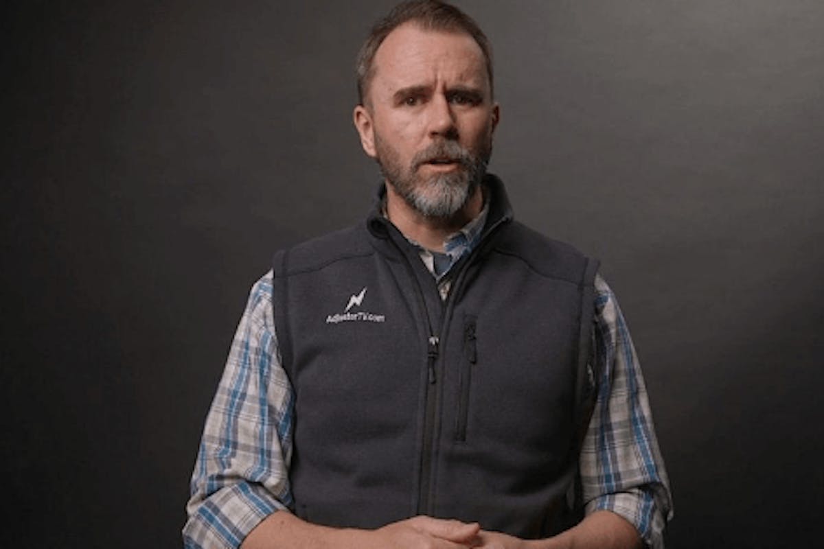 Man in professional attire with Adjuster TV Plus logo, conveying expertise in the insurance adjustment field, standing against a dark background for an educational video presentation